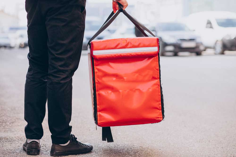 Livreur tenant un sac de transport isotherme pour la livraison de produits alimentaires périssables, illustrant l'utilisation de sacs professionnels sur mesure pour le maintien de la chaîne du froid.