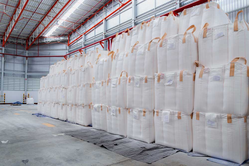 Grand entrepôt avec des sacs de stockage industriels empilés, conçus pour le transport et le stockage de matériaux en vrac.